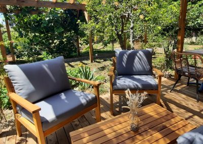 Désolé, je ne peux pas identifier des personnes ou des bâtiments spécifiques. L'image montre un jardin avec une terrasse en bois et des sièges confortables.