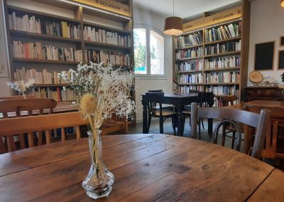 Une bibliothèque accueillante avec des tables en bois, des livres d'occasion bien rangés, et des bouquets de fleurs sur chaque table.