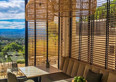 Une salle de restaurant élégante avec des lustres en rotin, des tables en marbre, et des pommes vertes. Vue sur la nature en arrière-plan.