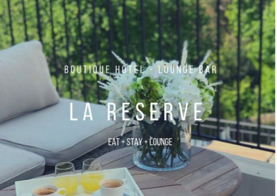 Un plateau de petit-déjeuner avec boissons sur une terrasse de l'hôtel La Réserve, entourée de végétation luxuriante. Ambiance détente.