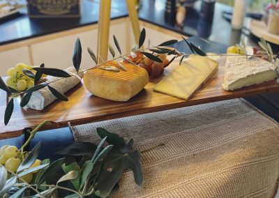Assiette en bois avec divers fromages, raisins et branche d'olivier. Cadre intérieur lumineux et élégant, ambiance gastronomique française.