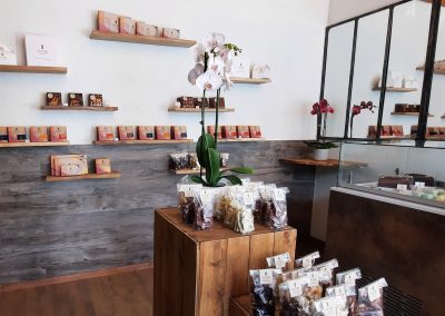 Boutique élégante avec des étagères de chocolat et de macarons colorés, ornée d'une orchidée au centre et décor moderne en bois et verre.