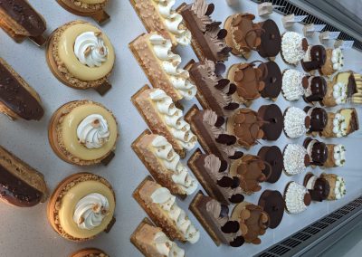 Assortiment coloré de pâtisseries françaises sur étagère réfrigérée, incluant tartes au citron, éclairs et gâteaux au chocolat soigneusement présentés pour les clients gourmands.