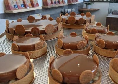 Pâtisseries brillantes sur plateau métallique dans une boutique élégante. Étagères avec chocolats en arrière-plan, ambiance gourmande et sophistiquée.