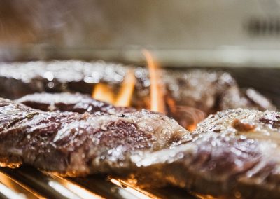Viande grillée sur le barbecue, avec des flammes visibles. L'image capte la cuisson en gros plan, texture juteuse et savoureuse. Aucune personne présente.