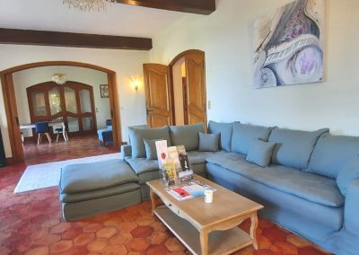 Un salon élégant avec canapé bleu, table basse en bois, carrelage ancien, œuvre d'art abstrait et portes en bois menant à la salle à manger.