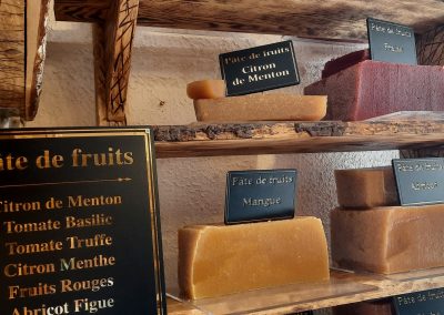 Des tablettes de pâte de fruits aux saveurs variées sont exposées sur des étagères en bois, étiquetées avec leurs arômes distinctifs.