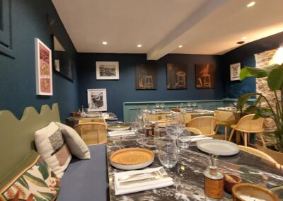 Un restaurant élégant avec des murs bleu marine, des tables en marbre, des chaises en rotin et des œuvres d'art modernes sur les murs.