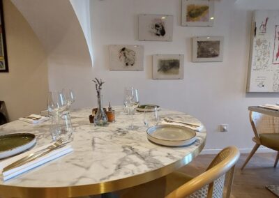 Un intérieur de restaurant élégant, avec une table en marbre rond, des chaises en bois clair et des œuvres d'art modernes sur les murs.