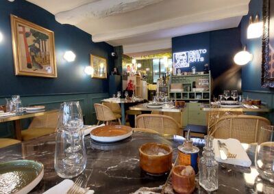 Un élégant restaurant avec des tables dressées, des œuvres d'art aux murs, ambiance chaleureuse. Décor moderne et accueillant, prêt pour les convives.