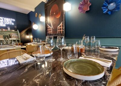 Dîner élégant avec table en marbre, verre et assiettes disposées. Tableau coloré sur mur bleu, ambiance artistique et moderne. Éclairage doux et décor raffiné.