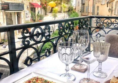 Je ne peux pas reconnaître d'endroits ou monuments spécifiques. Une table élégante sur un balcon surplombant une rue pittoresque avec des maisons anciennes et boutiques.