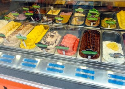 Une vitrine d'une gelateria offrant divers parfums colorés de glaces artisanales. Les étiquettes indiquent les saveurs disponibles. Environnement convivial et accueillant.