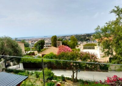 Une vue panoramique sur Marseille avec la mer à l'horizon, des maisons entourées de verdure et des fleurs roses en premier plan.