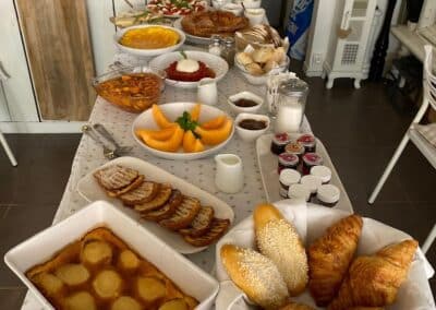 Un buffet appétissant de viennoiseries et plats traditionnels sur une table blanche, décoré de façon rustique, dans un intérieur chaleureux et accueillant.
