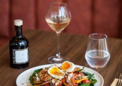 Une assiette de salade gourmande avec œufs, accompagnée de vin et eau sur une table en bois dans un restaurant élégant.