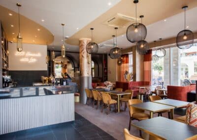 Un café moderne et élégant avec des tables en bois, des luminaires suspendus et un panneau "100% Homemade with Love" illuminé sur le mur.