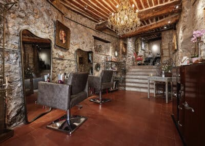 Une pièce élégante en pierre, avec des fauteuils de salon, un lustre somptueux, décorée de miroirs et peintures, ambiance chaleureuse et intime.