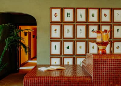 Une réception d'hôtel élégante, avec un comptoir en mosaïque rouge et des illustrations botaniques encadrées sur le mur derrière, éclairée par une lumière douce.