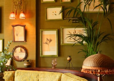 Une banquette vintage jaune dans un salon chaleureux, décoré de cadres et de plantes vertes, avec une lampe élégante éclairant l'espace.