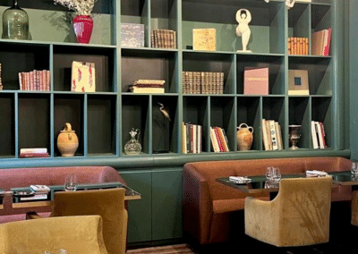 Un intérieur cosy avec étagères remplies de livres, objets d'art, et tables élégantes, créant une ambiance chaleureuse et raffinée pour les convives.