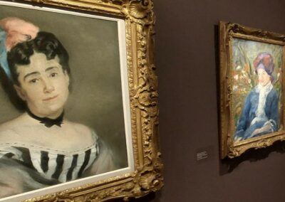 Deux peintures classiques avec cadres dorés sont accrochées sur un mur sombre dans une galerie d'art. Les portraits représentent des personnes élégantes.