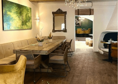 Une salle à manger élégante avec mobilier en bois, lustre, tableau vert, et miroir orné sur le mur. Atmosphère sereine et accueillante.