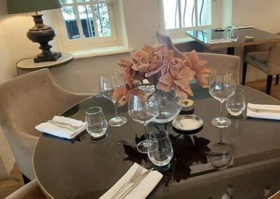 Une table élégante dans un restaurant, décorée de verres à vin, serviettes blanches et fleurs, avec une lumière douce d'une lampe.