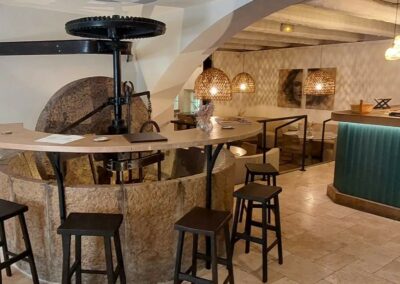 Un bar intérieur avec des sièges en bois et des décorations suspendues, offrant une atmosphère chaleureuse et accueillante. Tableau accroché au mur.