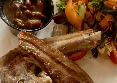 Un plat de côtes d'agneau grillées avec une sauce brune et une salade colorée de légumes frais, carottes et concombres.