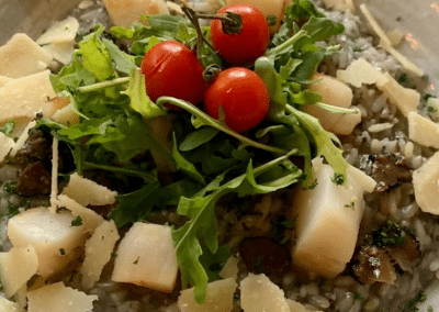 Assiette de risotto crémeux garnie de roquette, copeaux de fromage et tomates cerises, présentée dans un bol beige.