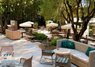 Espace extérieur élégant avec tables, parasols et arbres, ambiance estivale. Mobilier confortable, lumière douce et atmosphère paisible incitant à la détente en plein air.