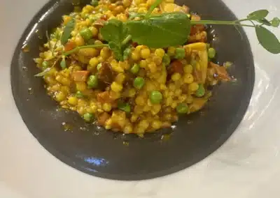 Un plat gastronomique avec des perles de couscous, petits pois et herbes fraîches, joliment présenté sur une assiette blanche.
