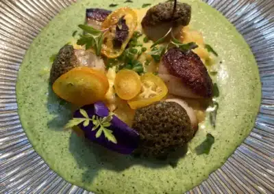 Un plat gastronomique avec des ingrédients colorés, préparé artistiquement, serti dans une assiette stylisée avec une sauce verte crémeuse.