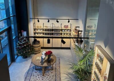 Boutique élégante avec étagères pleines de produits, un sapin de Noël décoré et une table ronde sur un tapis. Ambiance chaleureuse et accueillante.