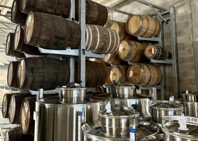 Barriques en bois et réservoirs en acier inoxydable dans une cave, créant une atmosphère de fabrication traditionnelle de spiritueux ou de vin.