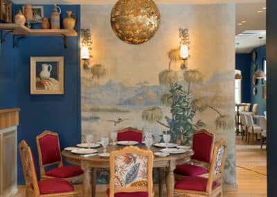 Une salle à manger élégante avec des murs bleus, un tableau mural, des chaises rouges, et des poteries décoratives sur une étagère.