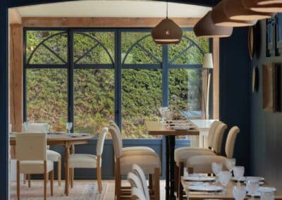 Un intérieur de restaurant élégant avec des tables dressées, des chaises confortables et de grandes fenêtres donnant sur un jardin verdoyant.