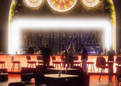 Cinq personnes discutent au bar illuminé d'un café moderne au décor vibrant avec des vitraux colorés au mur. Atmosphère chaleureuse et accueillante.