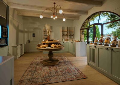Intérieur lumineux avec table garnie de pains et pâtisseries. Grande fenêtre voûtée offre vue sur arbres et jardin extérieur.
