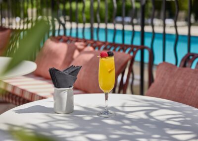 Une boisson à base de jus d'orange est posée sur une table près d'une piscine, entourée de sièges confortables et d'ombre.