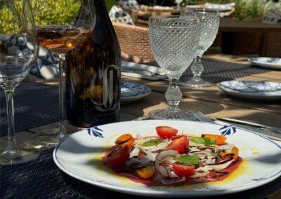 Un déjeuner élégant sur une table extérieure, comprenant du vin rosé, un plat de légumes colorés, et des verres à pied en cristal étincelants.