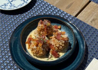 Une assiette de boulettes appétissantes garnies de morceaux de bacon, servie sur une nappe bleue à motifs. Atmosphère de déjeuner en plein air.