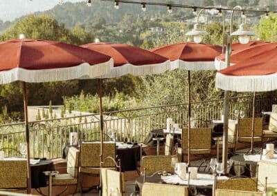 Un restaurant avec des parasols rouges sur une terrasse offrant une vue sur des collines verdoyantes, créant une ambiance paisible et charmante.