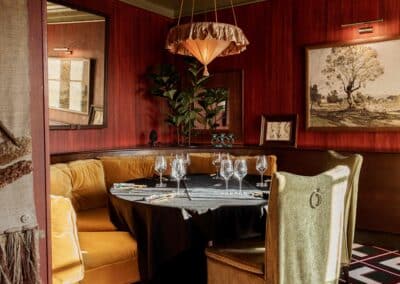 Un intérieur élégant d'un restaurant avec des banquettes jaunes, une table dressée, un lustre suspendu et des tableaux sur les murs en bois chaud.