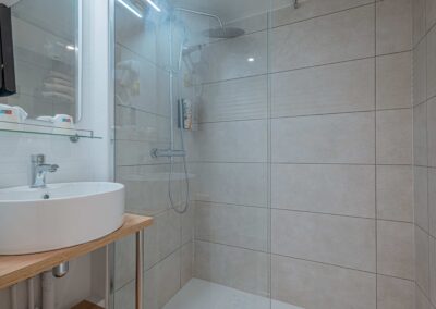 Salle de bain moderne avec douche à l'italienne, carrelage beige, lavabo blanc, miroir sur le mur, ambiance propre et lumineuse.